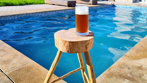 Een houten krukje met een glas bier bij een zwembad.