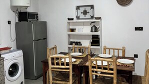 Een kleine keuken met een wasmachine, een koelkast en een eethoek met houten stoelen en een tafel.