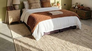 Een slaapkamer met een bed, gordijnen, een nachtkastje, een lamp, een dressoir en wanddecoratie.