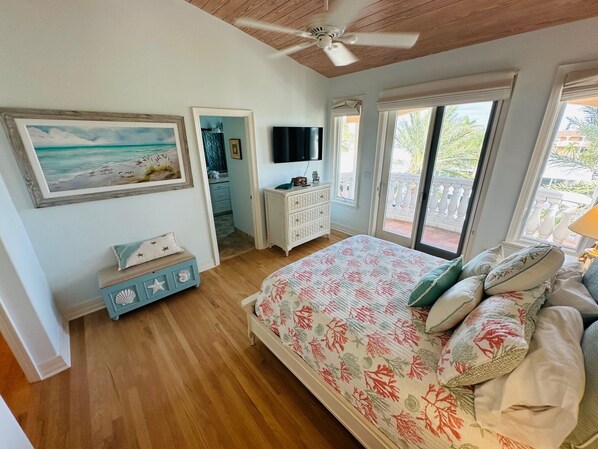 Une chambre avec un plafond en bois, un lit recouvert d’une literie à motifs floraux, une commode, un téléviseur et une vue sur l’extérieur grâce à une porte coulissante.