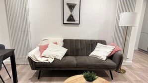 Una sala de estar moderna con un sofá marrón oscuro, cojines decorativos blancos y rojos con estampado, una pequeña mesa de centro redonda de madera con una planta en maceta y una obra de arte enmarcada sobre el sofá.