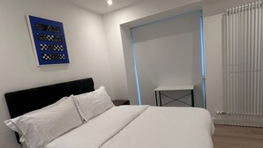 Un dormitorio moderno con cama, una mesita y una obra de arte colgada en la pared.