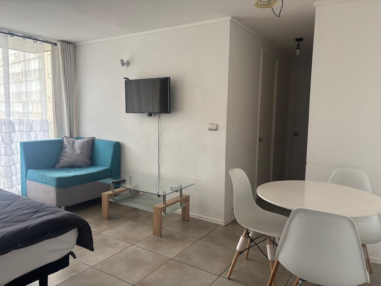 A modern hotel room with a glass table, a blue sofa, a bed, and a TV mounted on the wall.