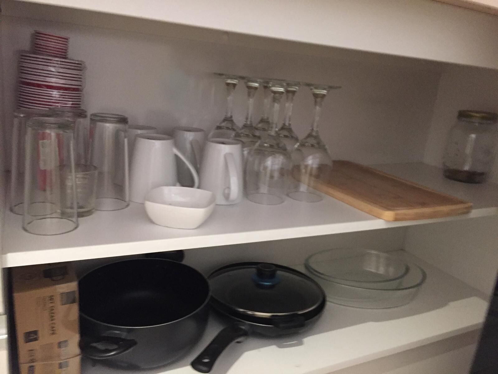 A kitchen shelf with various glassware, including wine glasses, a white bowl, and several glass jars.