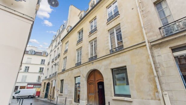 A narrow street with a building featuring a large wooden door and multiple windows. - Bridgestreet St Germain (Paris)