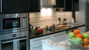 A modern kitchen with stainless steel appliances, a granite countertop, and a bowl of fruit. - Bridgestreet St Germain (Paris)