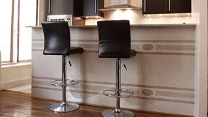 A modern kitchen with two black bar stools, a microwave, and cabinets. - Bridgestreet St Germain (Paris)