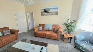 Ein Wohnzimmer mit braunem Sofa, blauem Sessel, Couchtisch und einem Bild eines Bootes an der Wand.