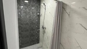 Eine begehbare Dusche mit Glastür, Marmorwänden und Fliesenboden.