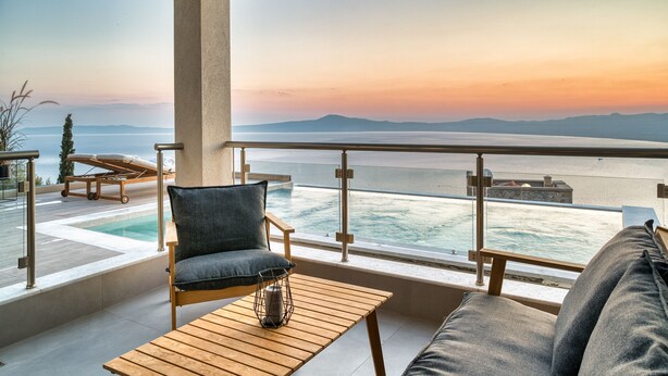 Un balcón con vistas al mar y a las montañas, una silla de descanso, un sofá y una mesa de madera.