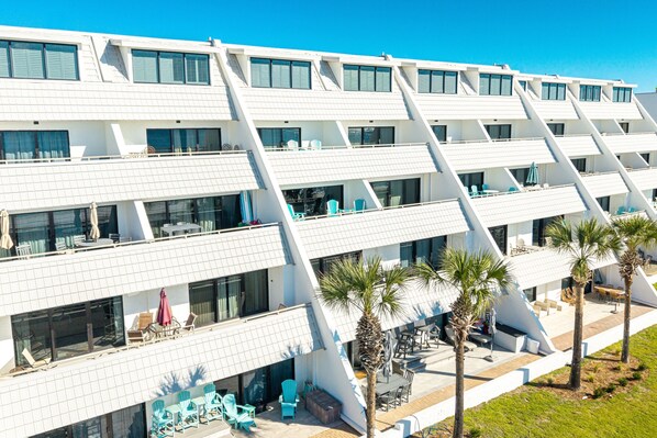 Un hotel moderno con varios balcones, mobiliario exterior y palmeras.