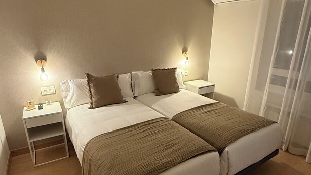 Un lit double avec deux oreillers, une table de chevet avec une lampe et une fenêtre avec un rideau.