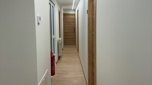 Un couloir avec un plancher en bois, des murs blancs et un extincteur sur le côté gauche.