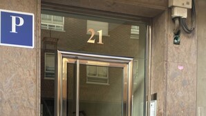 Une entrée d’immeuble avec une porte en verre, un panneau indiquant un parking (« P »), et le numéro « 21 » au-dessus de la porte.