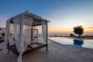 A serene outdoor setting with a wooden canopy bed, a pool, and a sunset view. - Villa Mediterranean View (Corfu)