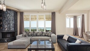 A modern living room with a large sectional sofa, a glass coffee table, and a fireplace. There are large windows offering a view of the sea. - Villa Mediterranean View (Corfu)