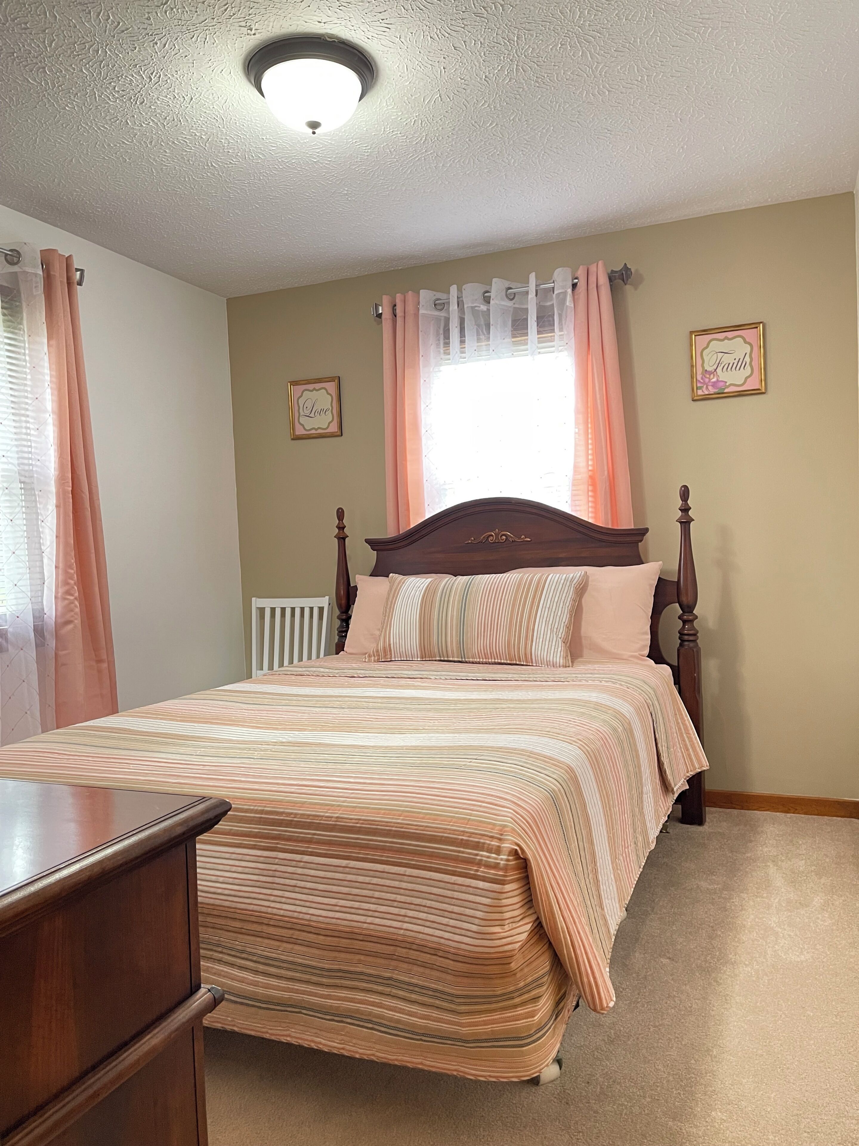 A bedroom with a wooden bed, a nightstand, a window with curtains, and two wall decorations.