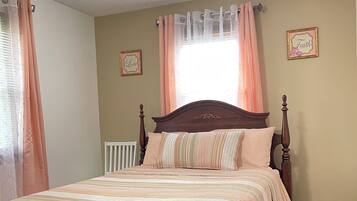 A bedroom with a wooden bed, a nightstand, a window with curtains, and two wall decorations.