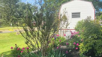 A white building with a red trim, surrounded by a garden with pink flowers and green plants.