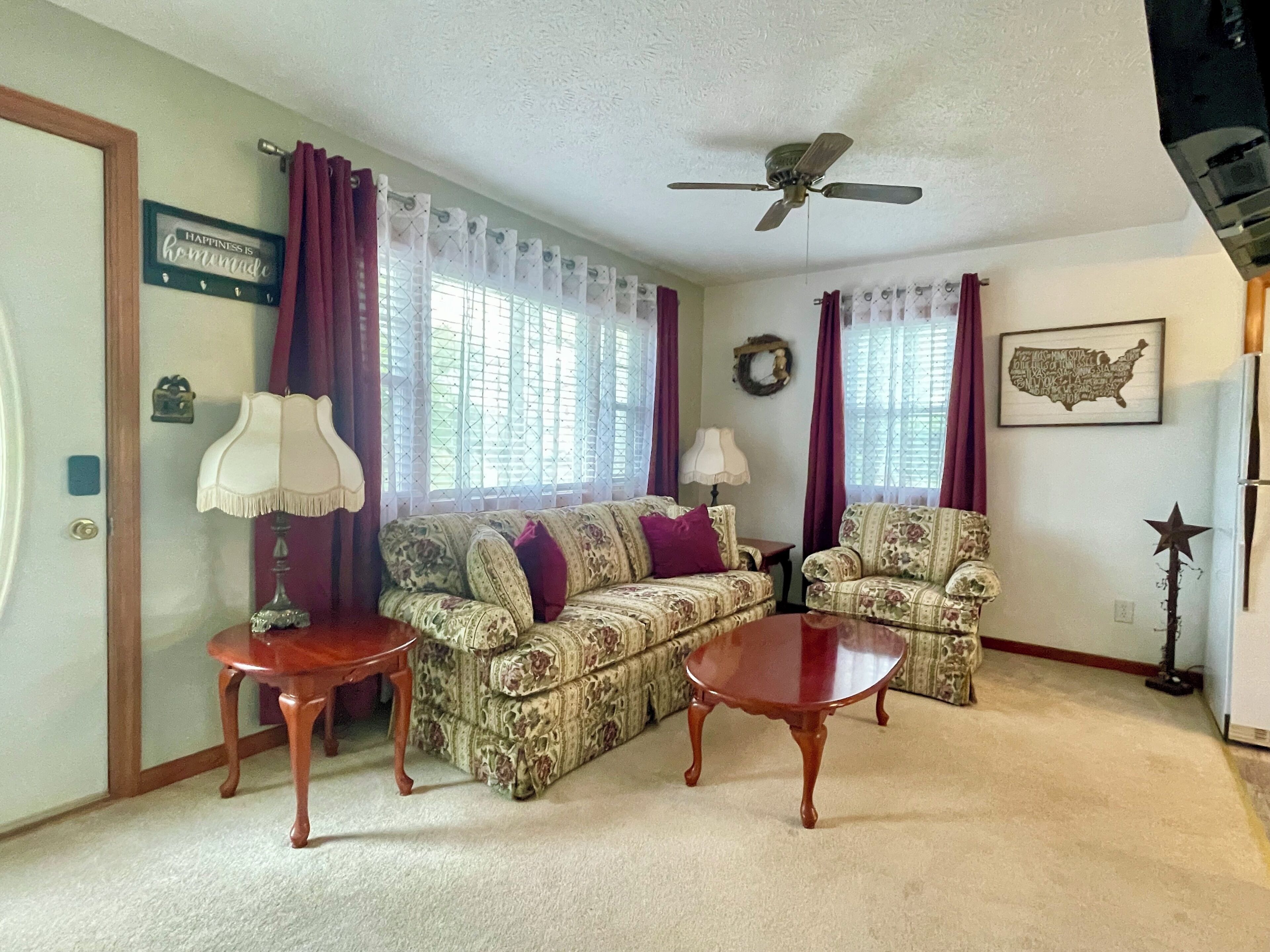 A living room with two patterned sofas, a wooden coffee table, a ceiling fan, and a wall-mounted map.