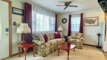 A living room with two patterned sofas, a wooden coffee table, a ceiling fan, and a wall-mounted map.