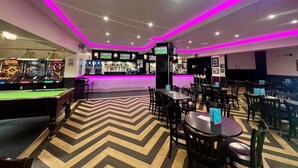 Zona de bar con mesa de billar, varios arreglos de asientos y barra con pantalla de televisión.