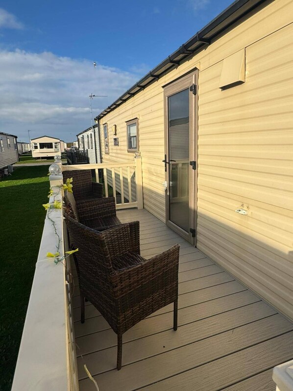 A row of mobile homes with a porch area featuring wicker furniture. - Olivia Caravan Sleeps 6 With Wi-fi (Rhyl)