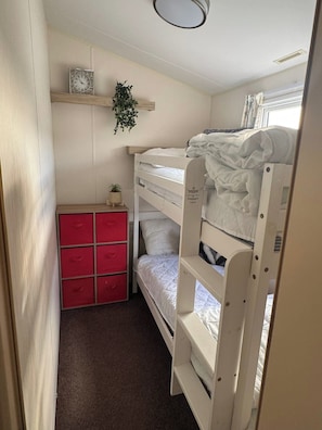 Habitación con literas, un mueble de almacenamiento rojo y una pequeña estantería con una planta.