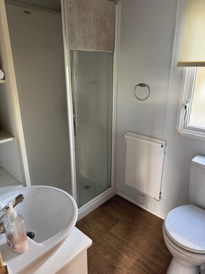 Kylpyhuone, jossa on lasiseinällä varustettu suihku, valkoinen pesuallas ja wc.
