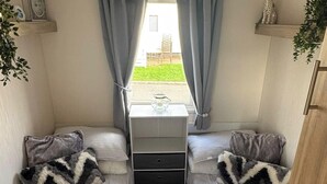 Un dormitorio pequeño con dos camas individuales, un tocador y una ventana con cortinas.