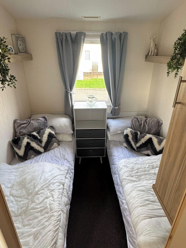 Un dormitorio pequeño con dos camas individuales, un tocador y una ventana con cortinas.