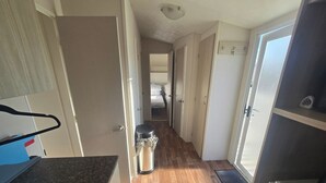 A narrow hallway with wooden flooring, a trash bin, and a door leading to a bedroom.