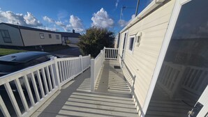 A wooden deck leading to a beige mobile home with a white railing.