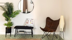 A room with a potted plant, a round mirror, a bench with a patterned pillow, a brown leather chair, and a tall floor lamp. - Home of Petros | Near Plaka - Temple of Zeus View (Athens)