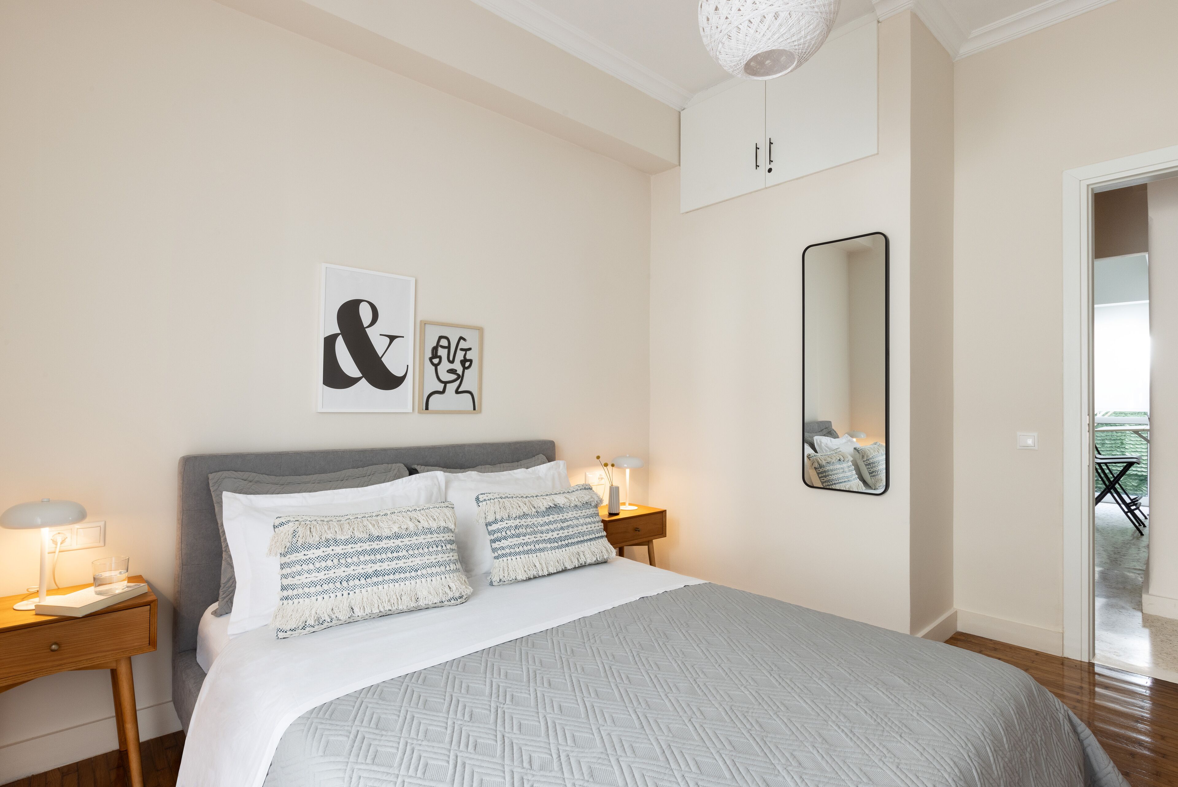 A bedroom with a bed, bedside tables, a mirror, and artwork on the wall.