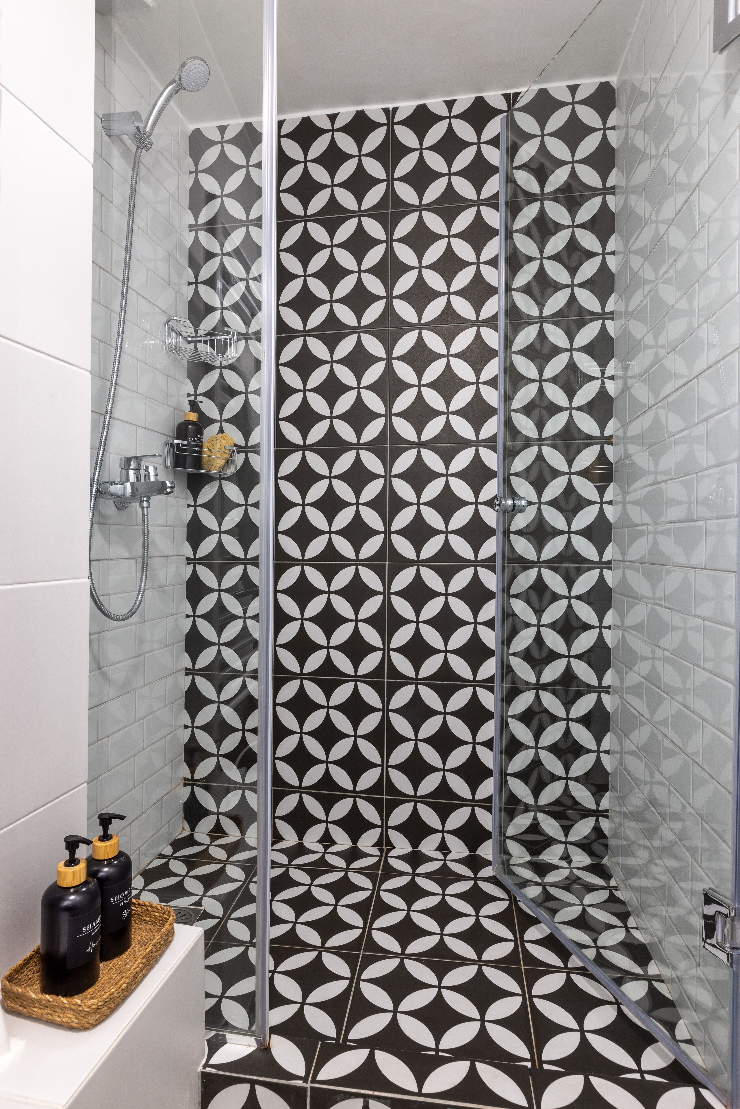 Una ducha con un diseño geométrico de azulejos, una puerta de cristal y un estante con artículos de aseo.