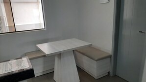Une petite pièce moderne avec une table et un banc blancs, une fenêtre et une porte.