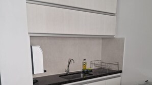Une cuisine de taille réduite avec des meubles blancs, un plan de travail noir, un évier en acier inoxydable et une cuisinière à gaz.