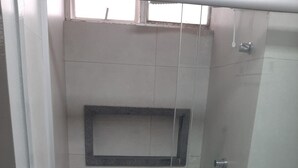 Une petite cabine de douche fermée, dotée d’une porte en verre, de toilettes blanches et d’une étagère au-dessus de la douche.