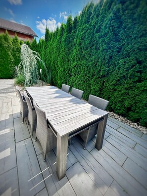 Relax on the patio surrounded by lush greenery and enjoy meals at the rectangular table with comfortable wicker chairs.