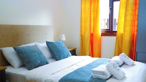 A neatly made bed with blue and white bedding, a bedside lamp, and a window with orange curtains. - Edinburgh Mansion Retreat (Edinburgh)