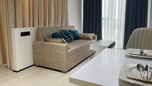 Una habitación de hotel moderna con un sofá color beige, una mesa de comedor con platos y cubiertos, y una pequeña mesita auxiliar blanca.