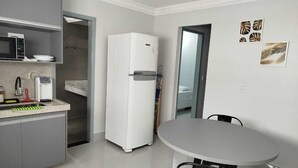 Une cuisine moderne avec un réfrigérateur blanc, un four à micro-ondes encastré et un évier. On y trouve également une table à manger avec des chaises.
