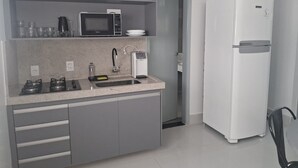 Une cuisine compacte équipée d’un four à micro-ondes, d’une cuisinière à gaz, d’un évier et d’un réfrigérateur blanc.