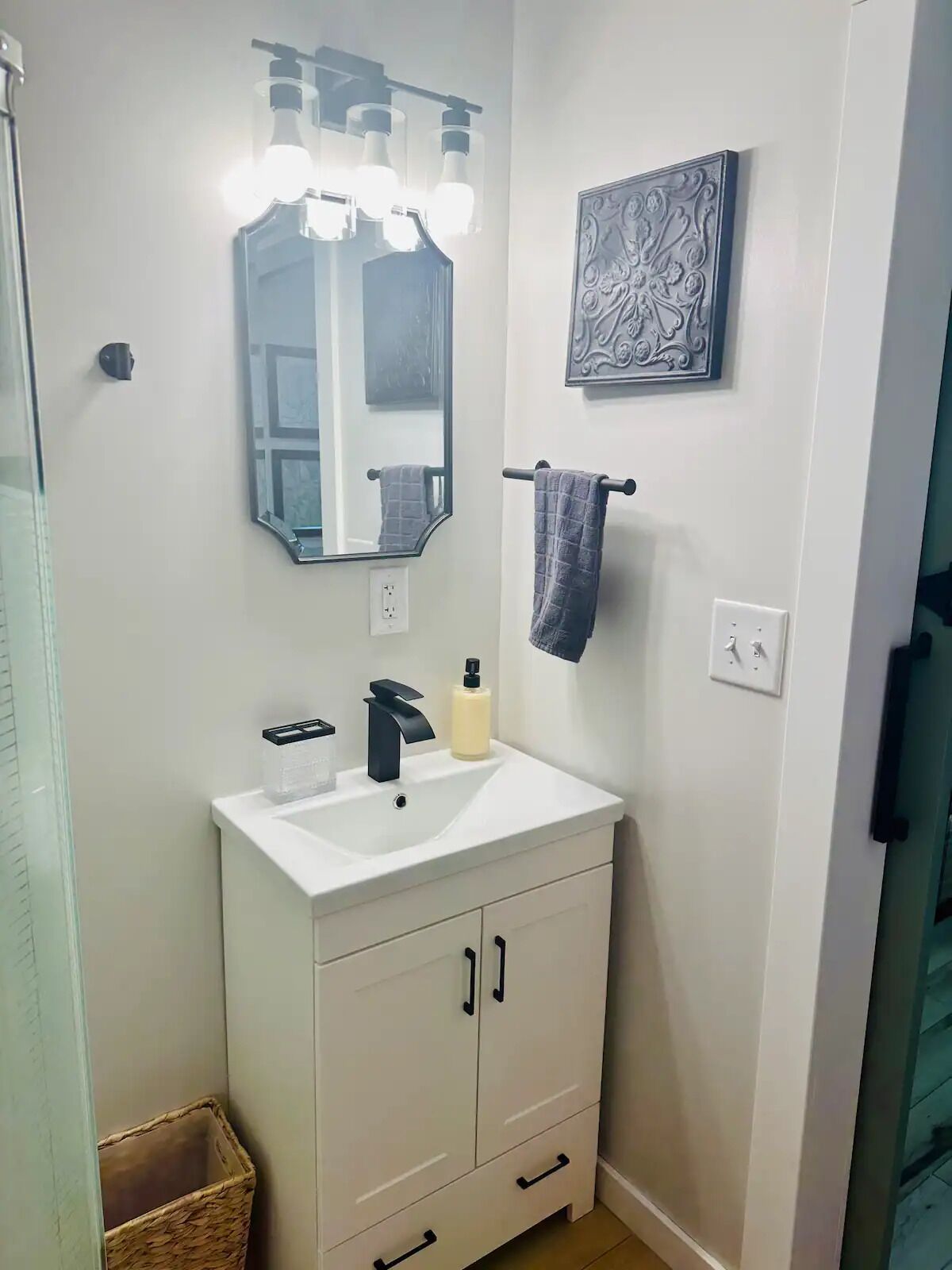 A bathroom with a white sink, a mirror, a towel rack, and a decorative wall piece.