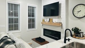A modern kitchen with a flat-screen TV, a clock, and a sink. - Sunset Tiny House Retreat | Fire Pit & Starry Sky (Logan)