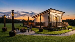 A two-story house with a deck, outdoor seating, and a fire pit. - Sunset Tiny House Retreat | Fire Pit & Starry Sky (Logan)