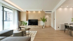 Ein modernes Wohnzimmer mit einem Flachbildfernseher, einem Essbereich mit Tisch und Stühlen sowie einem großen Fenster, das für natürliches Licht sorgt.