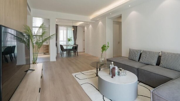 Ein modernes Wohnzimmer mit einem grauen Sofa, einem runden Couchtisch und einem Essbereich mit einem Glastisch und Stühlen.