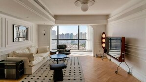 Ein großzügiges Wohnzimmer mit einem großen Fenster, einem Sofa, einem Couchtisch und einem Fernseher auf einem Schrank.